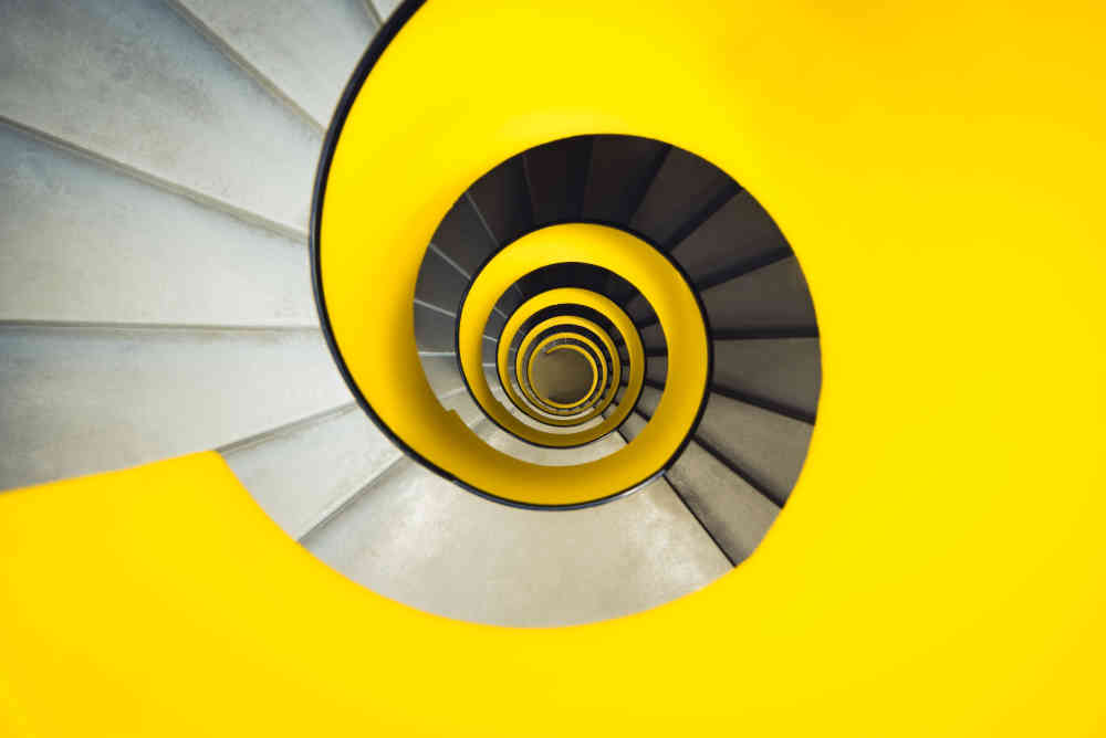 Looking straight down concrete spiral starircase whose interior guard wall is yellow on the outside